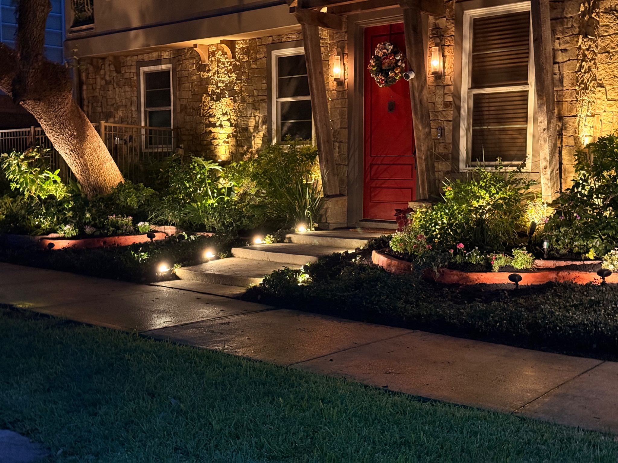 Professional landscape lighting on stone house with red door in Upper Kirby Houston - path lights and architectural uplighting